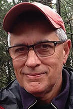 Mills Kelly in a red baseball cap standing in front of pine trees