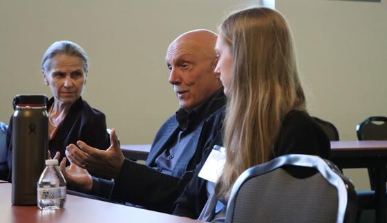 Stu Shea talking with hand motions while Zofia Burr and a student watch attentively