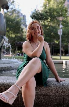 Portrait of Cece Foye with her legs crossed in front of a fountain